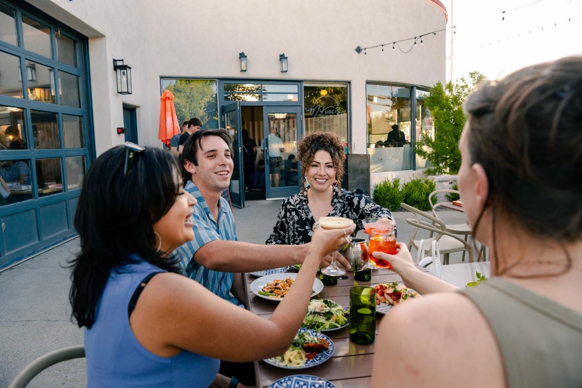 Four people "cheers" their drinks on the patio of M'tucci's Bar Roma