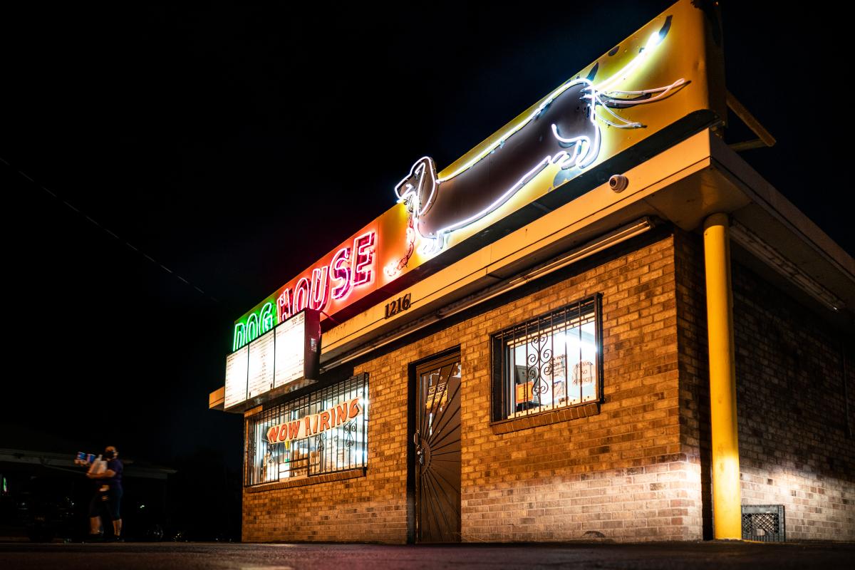 The exterior of The Dog House in Albuquerque at night. It is a brick building with a green and red neon sign that says "dog house" and a neon dachshund.