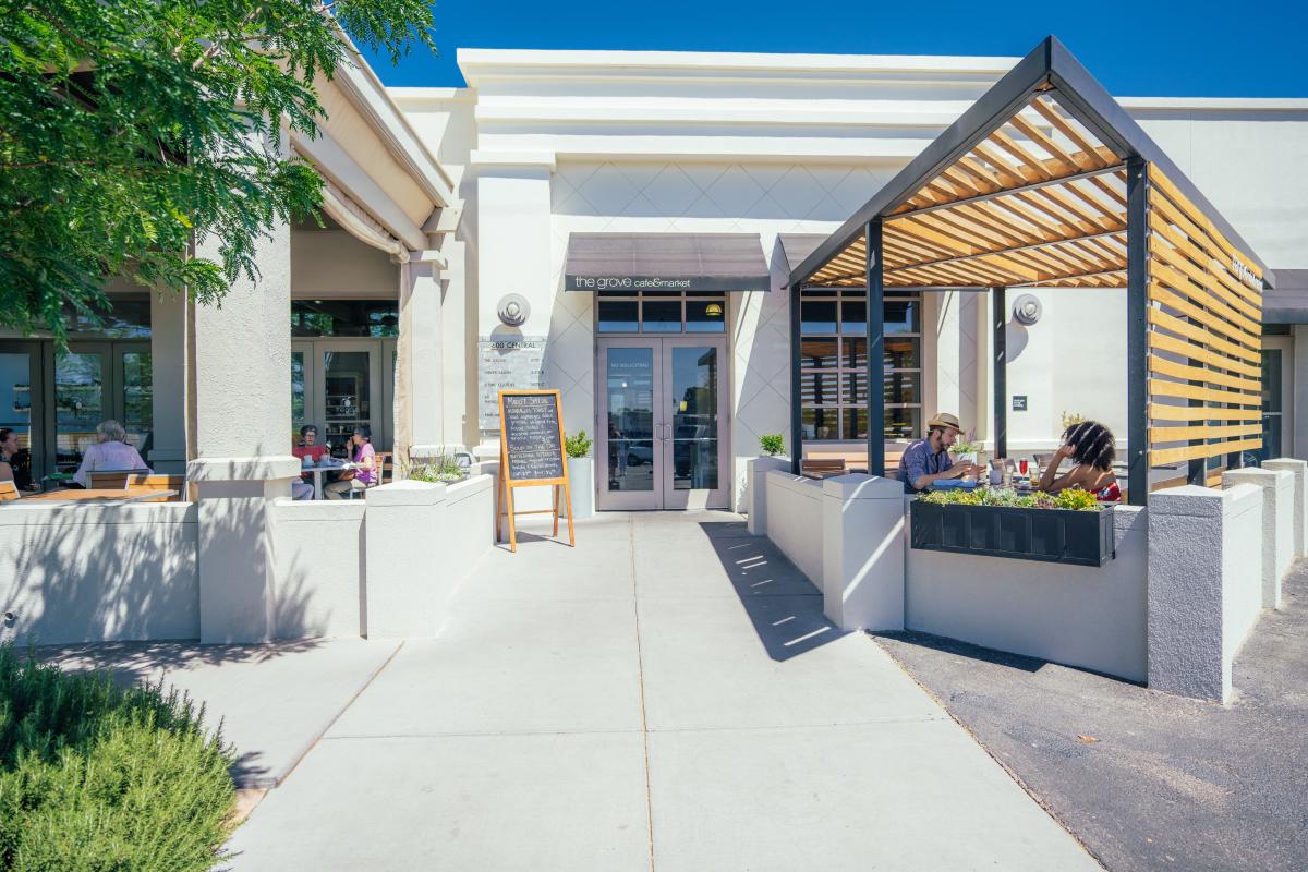A photo of the entrance to The Grove Cafe and Market. It is a white building with some outside tables.