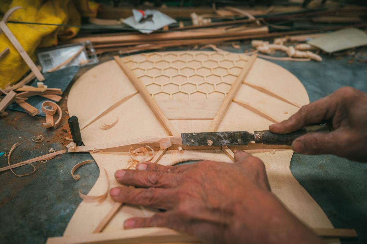 One of the Pimentel brothers uses a tool to shave wood off of a guitar being built.
