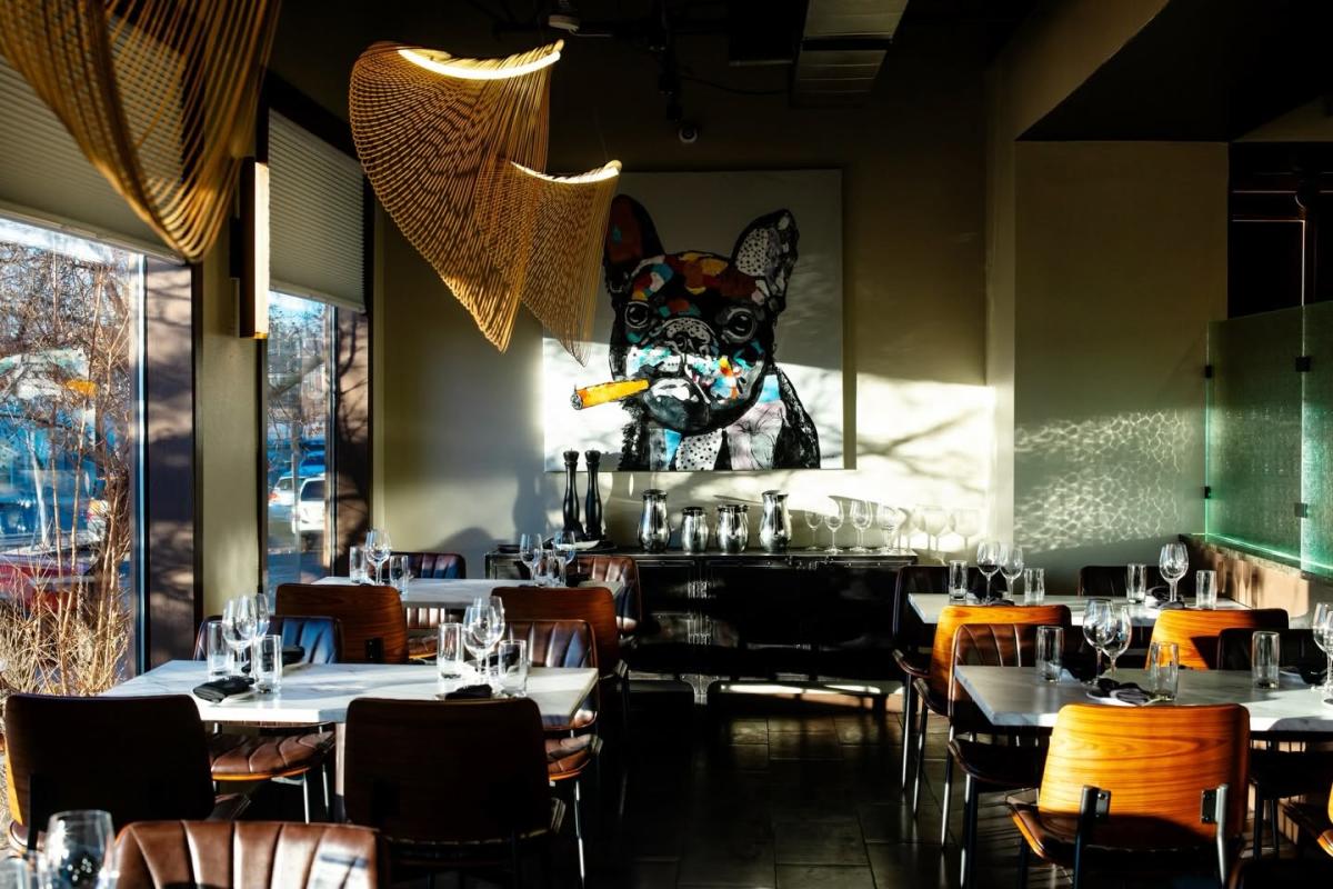 A photo of the interior of Pazzi Ristorante Italiano. There are tables set with wine glasses and silverware. A painting of a French bulldog smoking a cigar is on the wall.