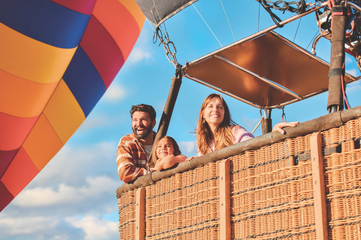 A mom, dad and daughter ride in the basket of a hot air balloon.