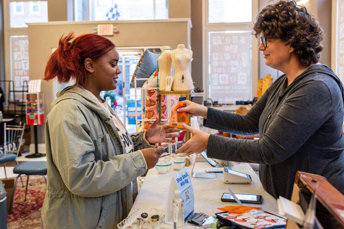 A black woman with red hair pays for a gift purchased by a local merchant.