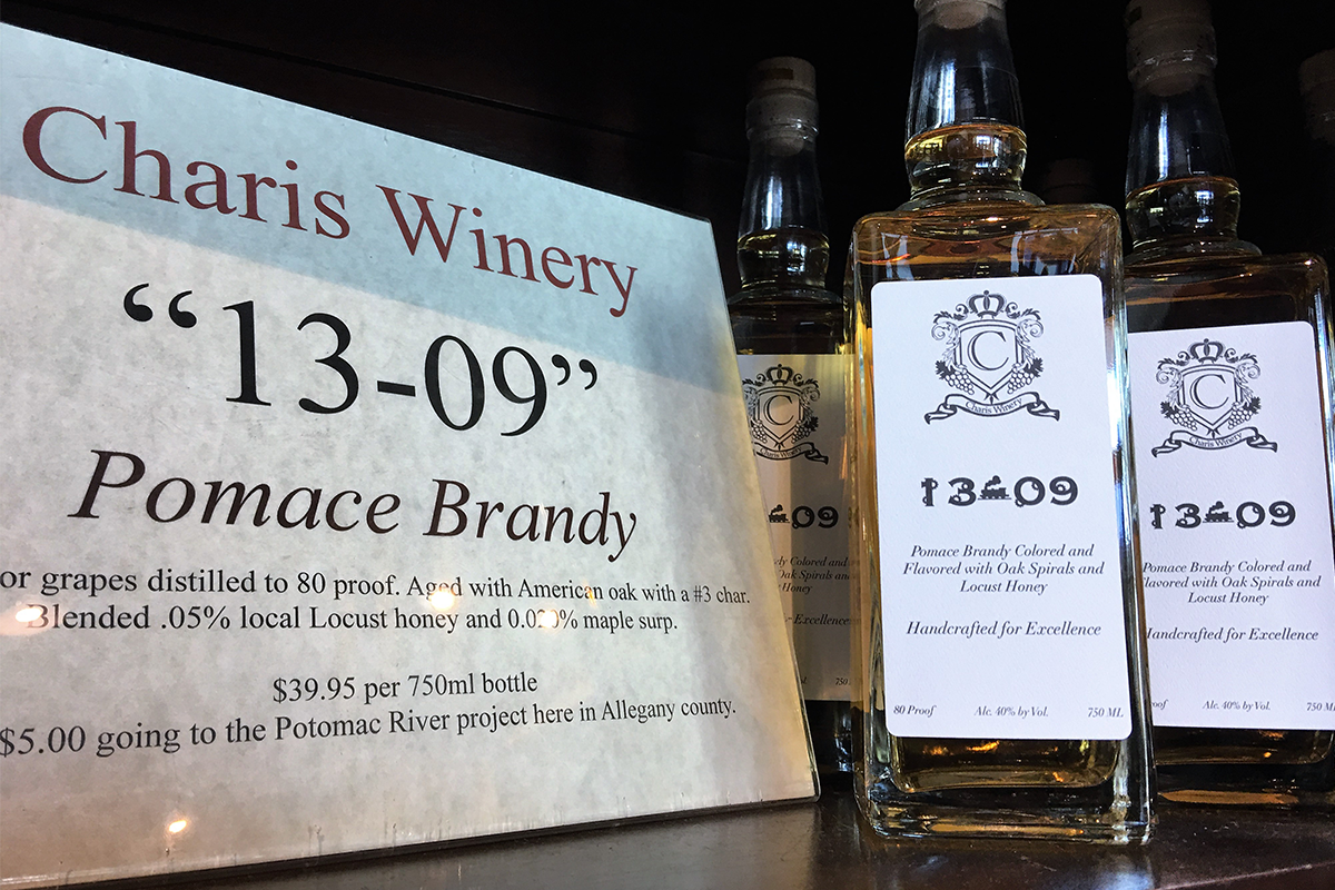 A sign that says "Charis Winery 1309 Pomace Brandy" sitting next to two bottles of 1309 Pomace brandy.