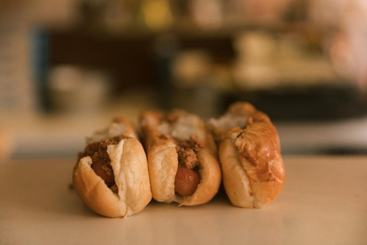 Three hot dogs topped with sauce and diced onions lined up on a counter.
