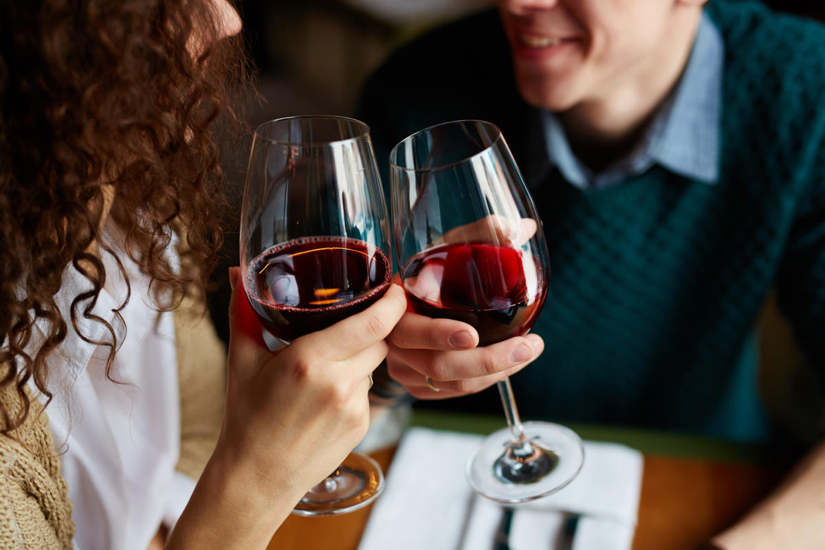 Couple clinking glasses of red wine during a cozy date night at a restaurant.
