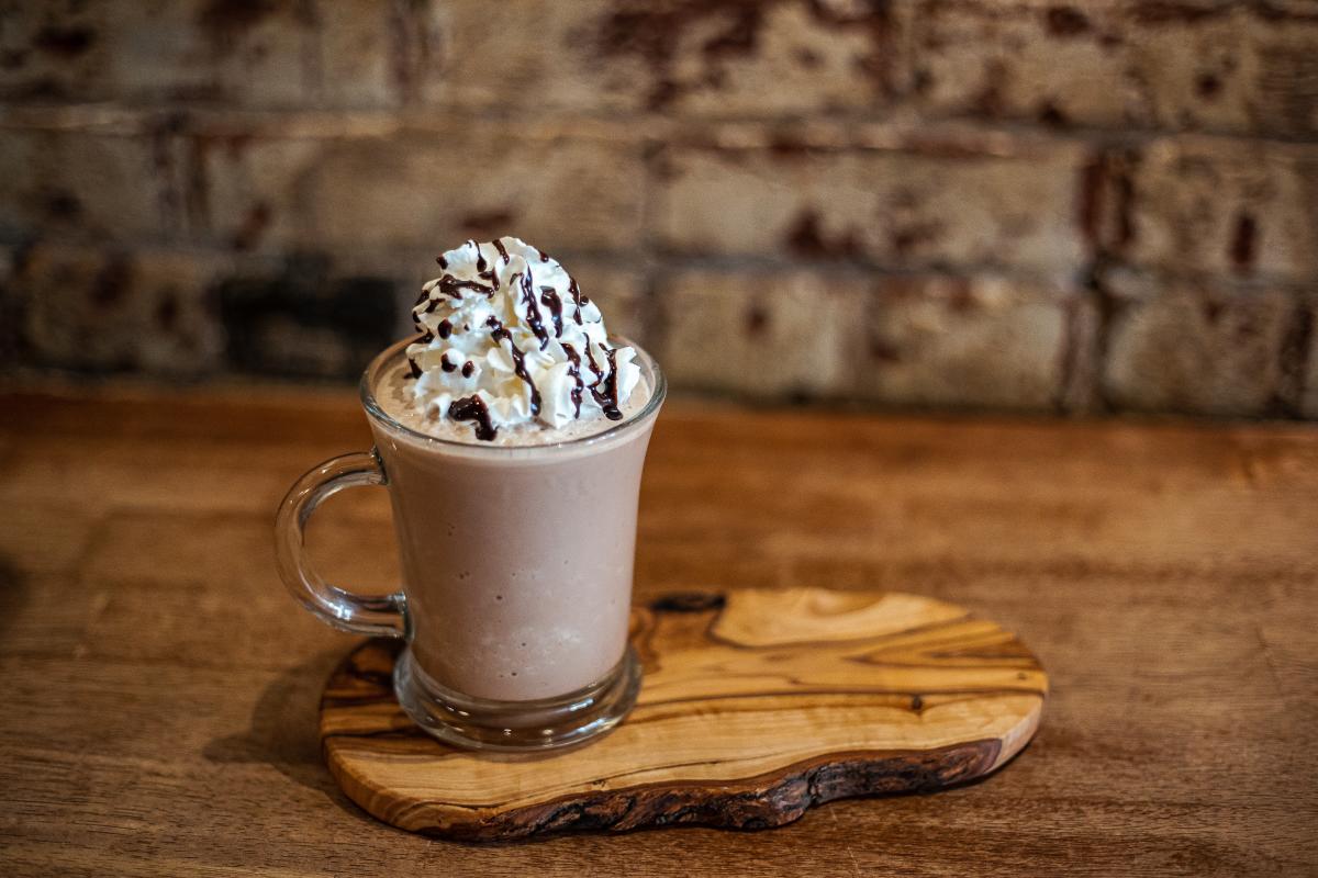 A coffee drink with whipped cream and chocolate syrup sits on a wooden serving board.