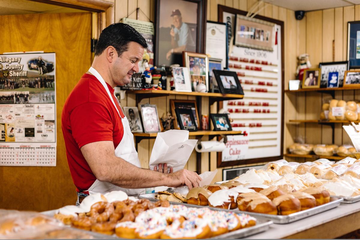 A man in a red shirt grabs a donut to put in a bag for a customer.