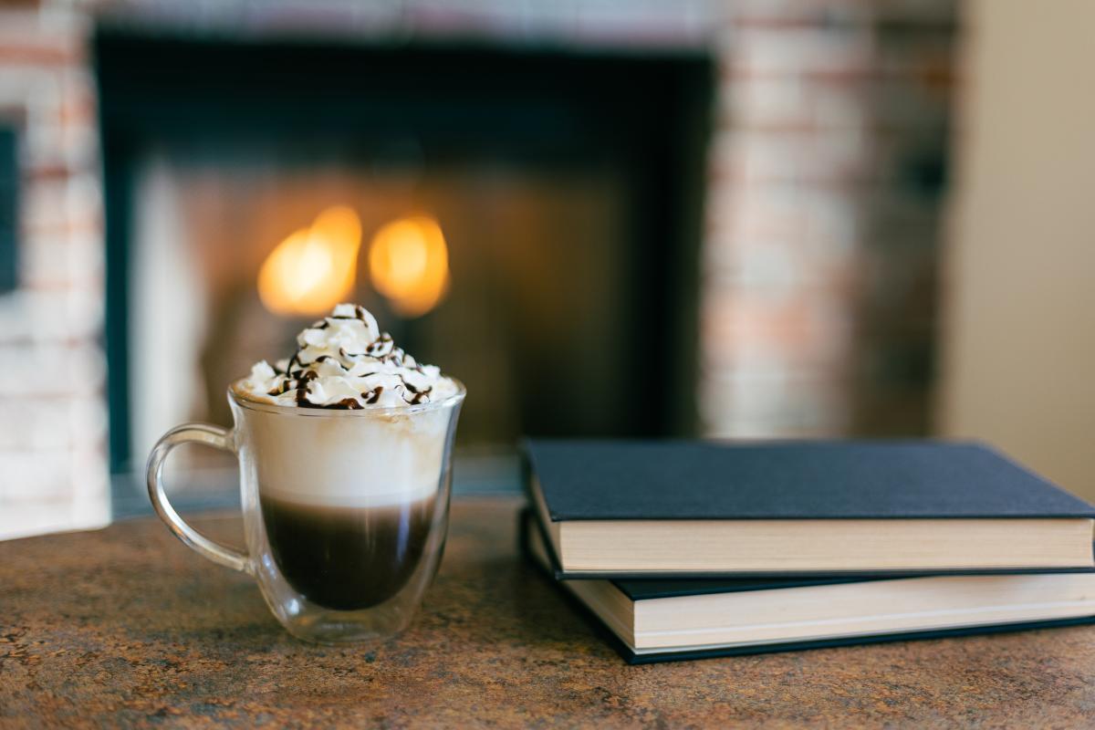 An espresso with cream and whipped cream sits on table next to two books.