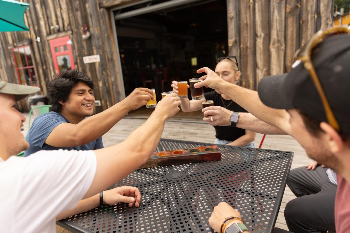 A group of adults sit around a table, holding up glasses of beer to cheers eachother.