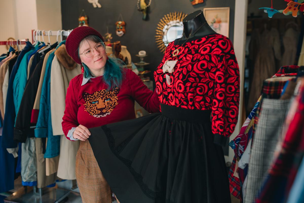 A woman with a red hat and vibrant blue hair displays a red and black top and black shirt outfit on a mannequin.