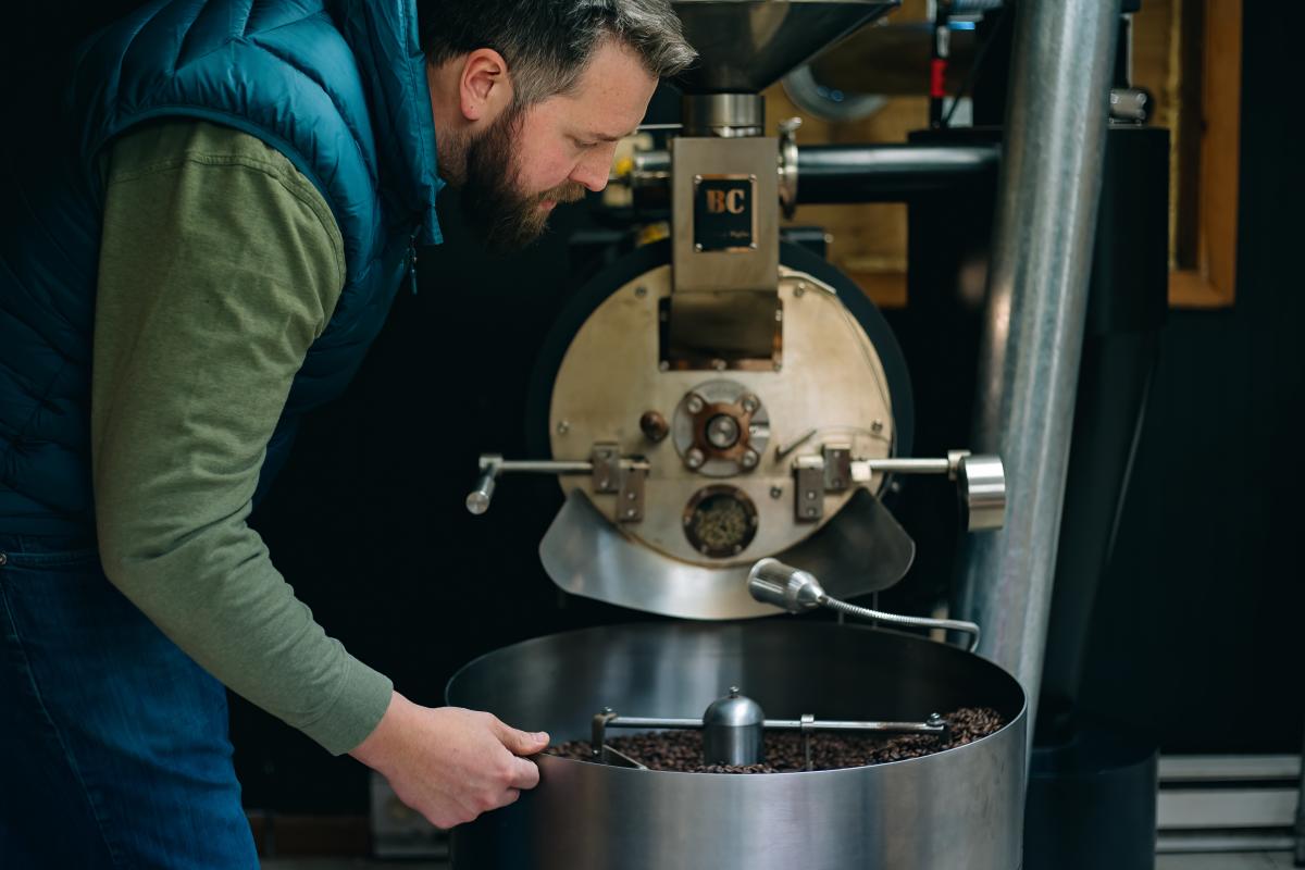 A man pulls a handle on a large coffee roaster machine.