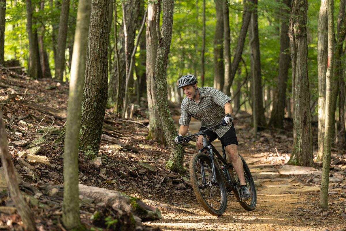 A man rides a bike on a rough mountain trail through the woods.