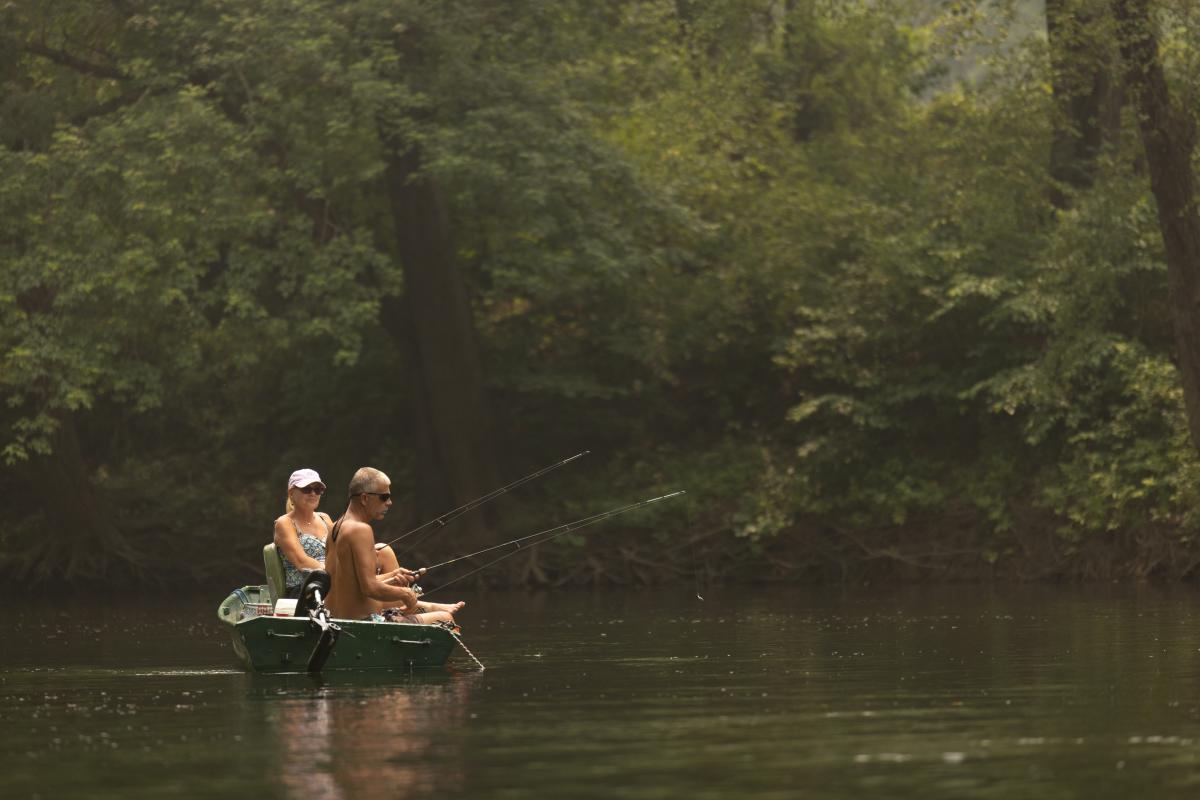 Two people fishing from a small boat on the Potomac River near Cumberland, Maryland, surrounded by wooded shoreline