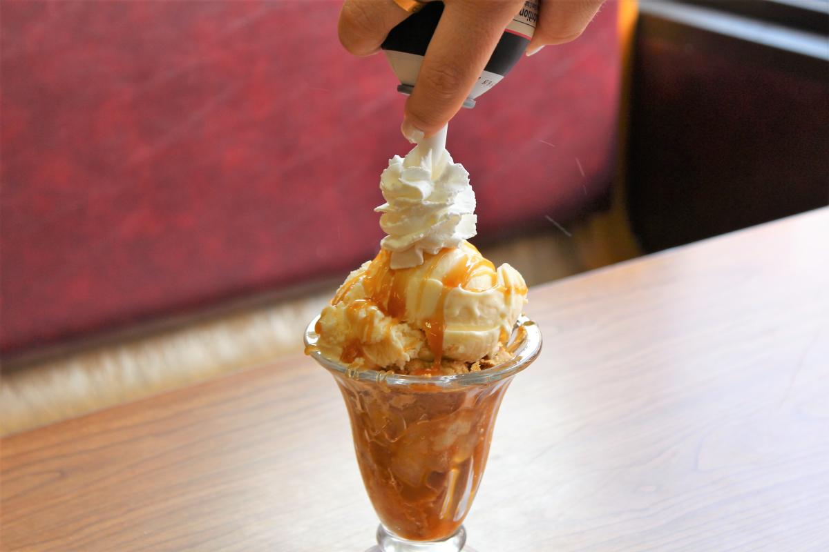 Someone adds whipped cream topping to the top of an apple pie sundae creation.