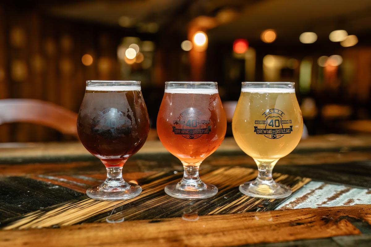 A flight of three beers ranging in color from brown, to amber, to gold lined on a bar top.
