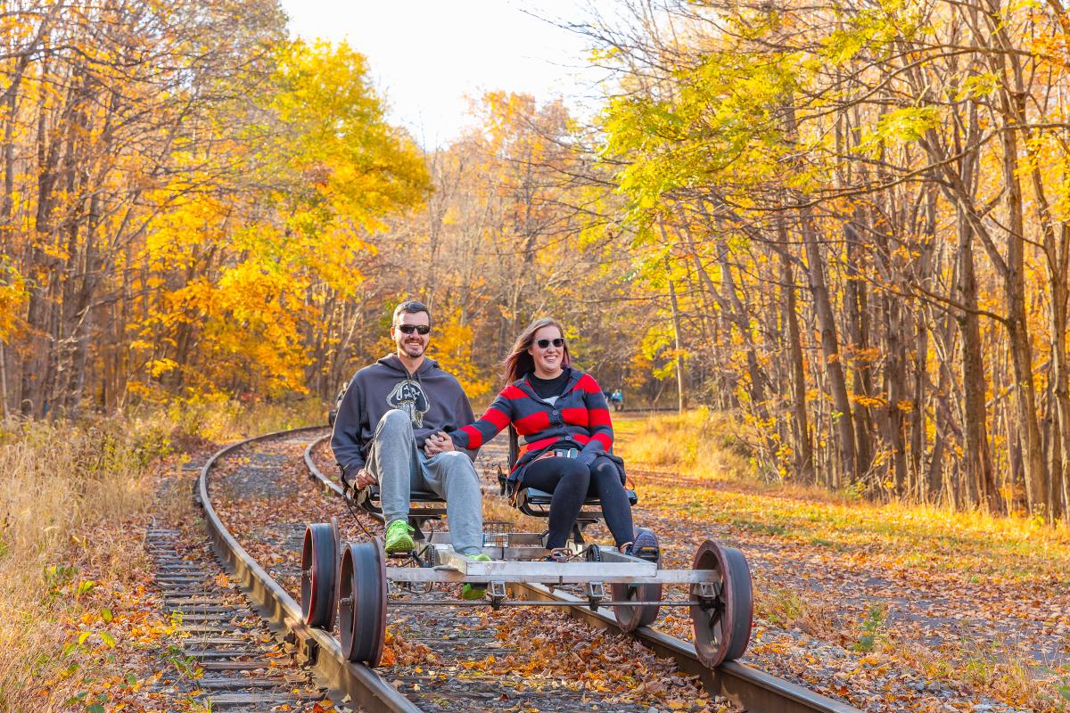 A couple peddles on a rail bike riding along the rail line in the fall.