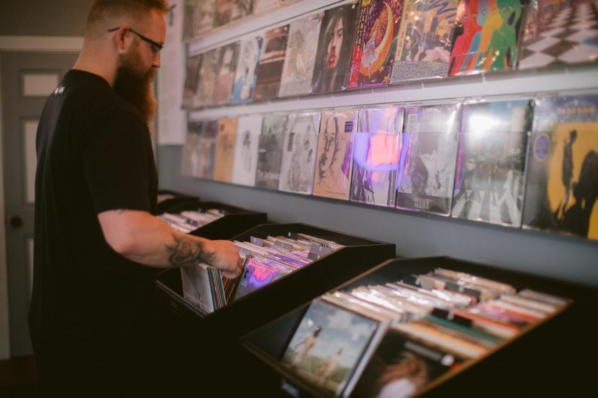 A man stands in front of a display, looking through a box full of vinyl records.
