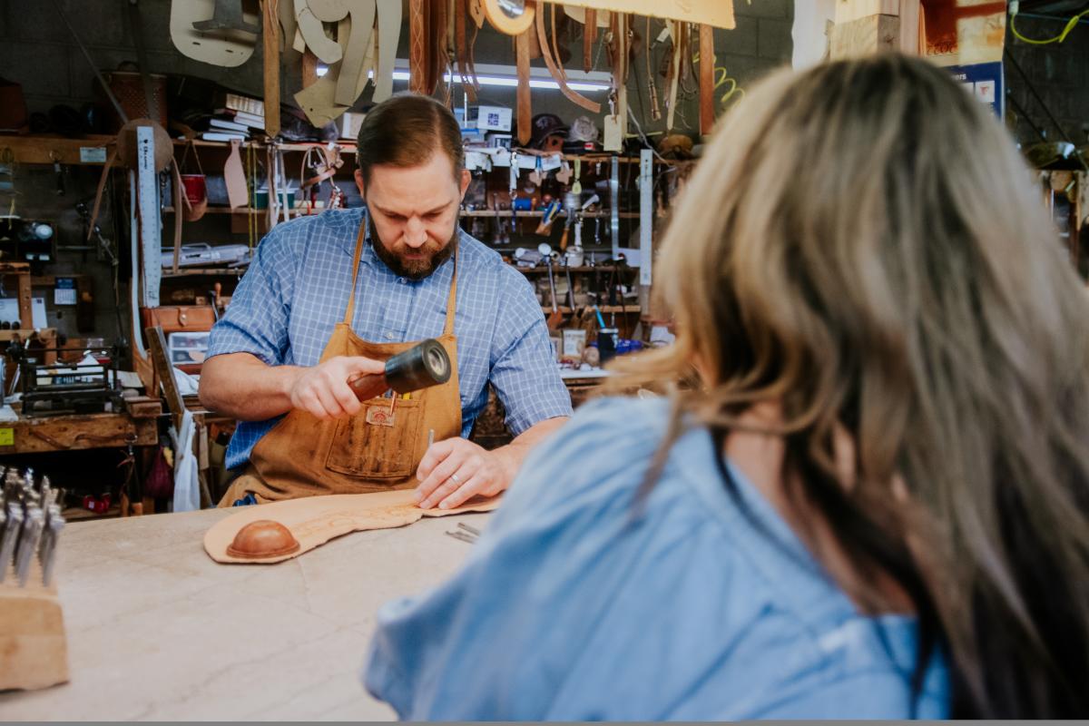 Woman watching man work on leather at Olivers Saddle Shop