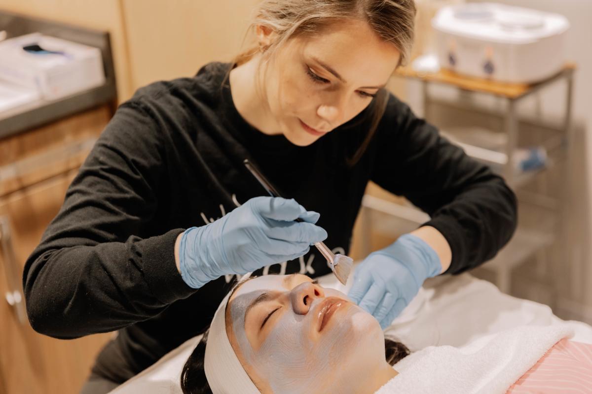Aesthetician applying face mask on woman