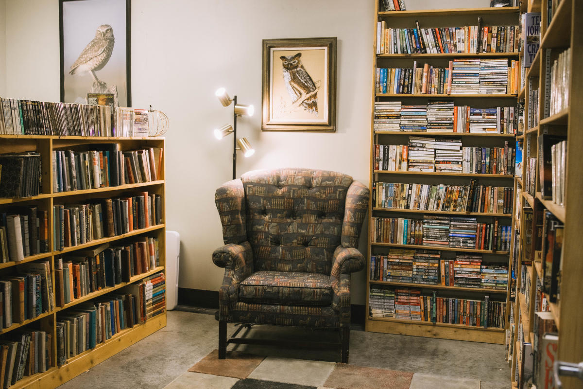 Corner of a bookstore with a chair with book print and two large shelves full of books