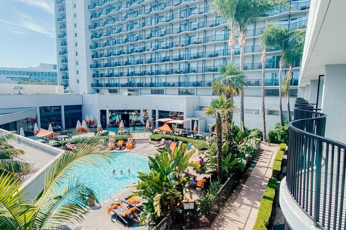 Image of the pool area at the Anaheim Marriott hotel. The photo shows a pool lined with seats and palm trees. The background is the Anaheim Marriott hotel.