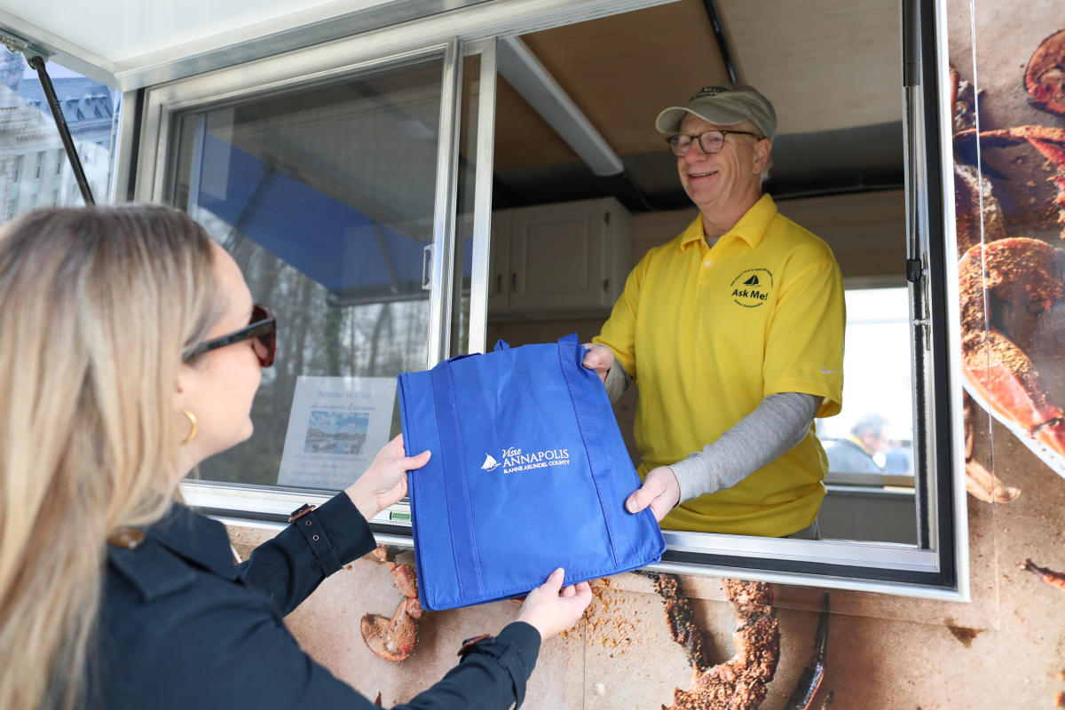 A man hands a woman a visitors guide and tote bag.