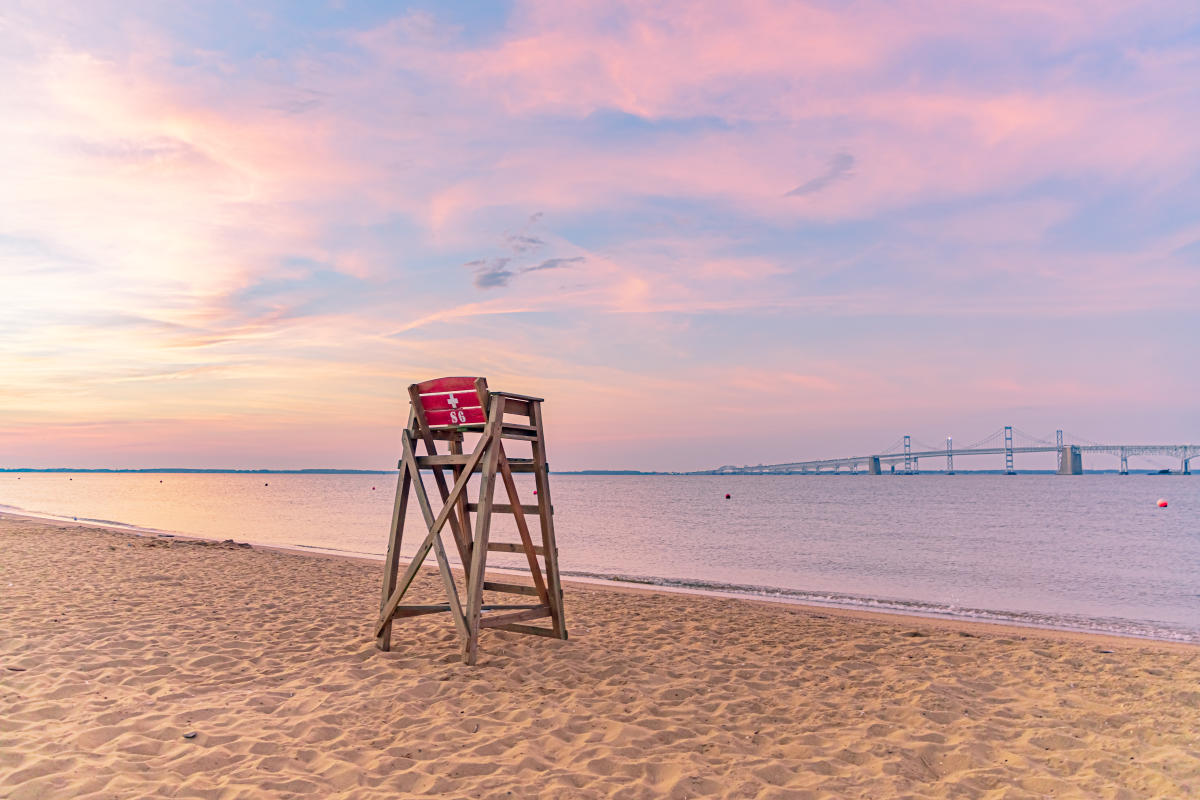 a lifeguard chair on a deserted beach at sunrise with the Bay Bridge on the horizon