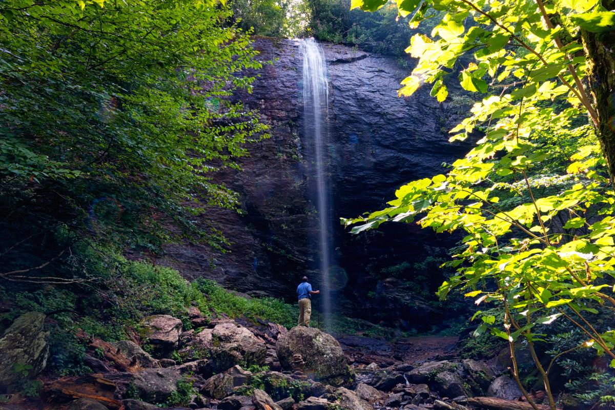 Man standing at the bottom of waterfall in the middle of the forest at Douglas Falls