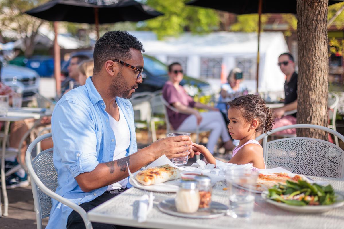 A man and his daughter sit at an outdoor table, eating.