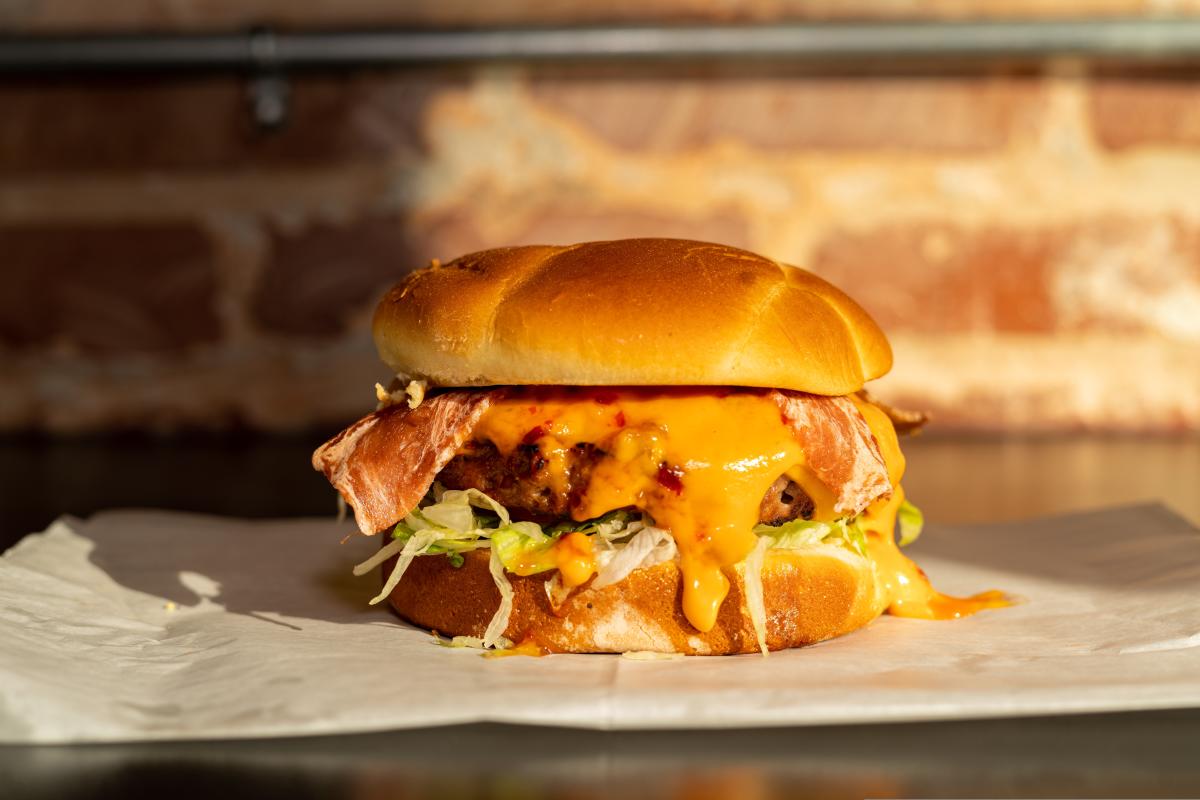 A delicious looking plant-based burger sits on a table in front of a brick background.