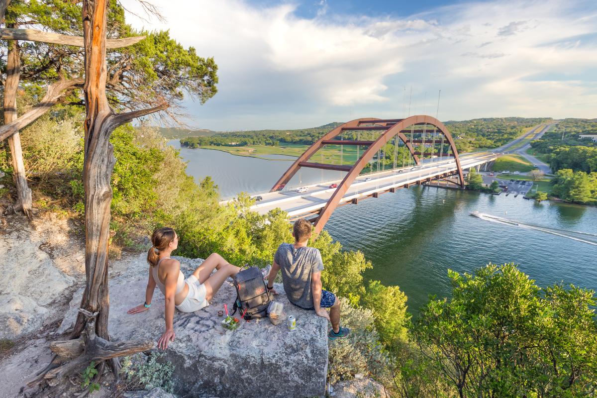 Hikers sitting on a hilltop rock overlooking the Pennybacker Bridge at Lake Austin.
