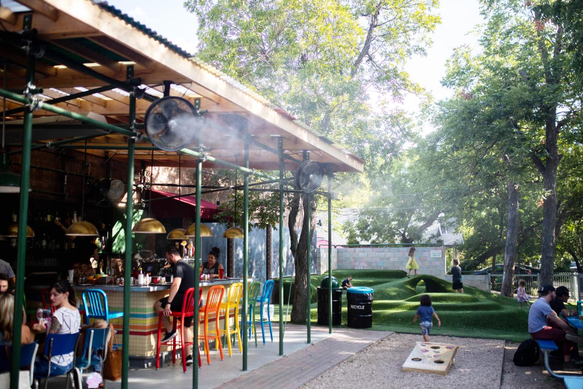 Image of the outdoor space at Home Slice Pizza featuring a bar with colorful chairs and a hilly greenspace with kids playing.