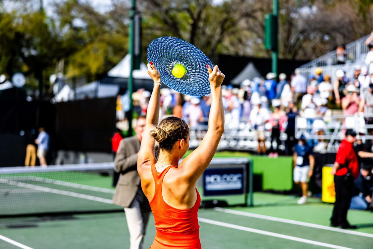 Female tennis player holding a disc shaped trophy above her head in front of a crowd.