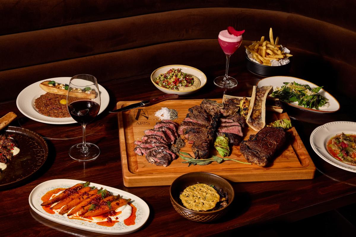 A spread of steak and other side dishes sitting on a table at Aris.