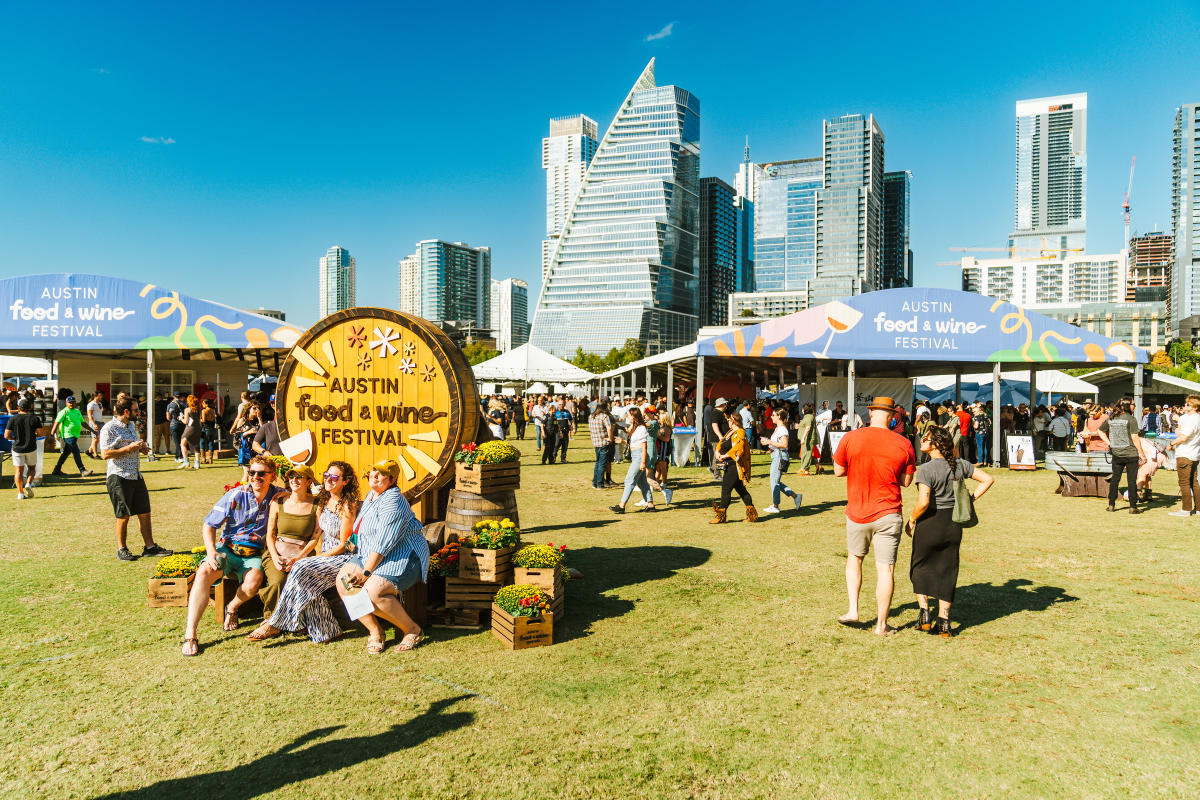 Image of people attending the Austin Food + Wine Festival at Auditorium Shores with the downtown skyline in the background.