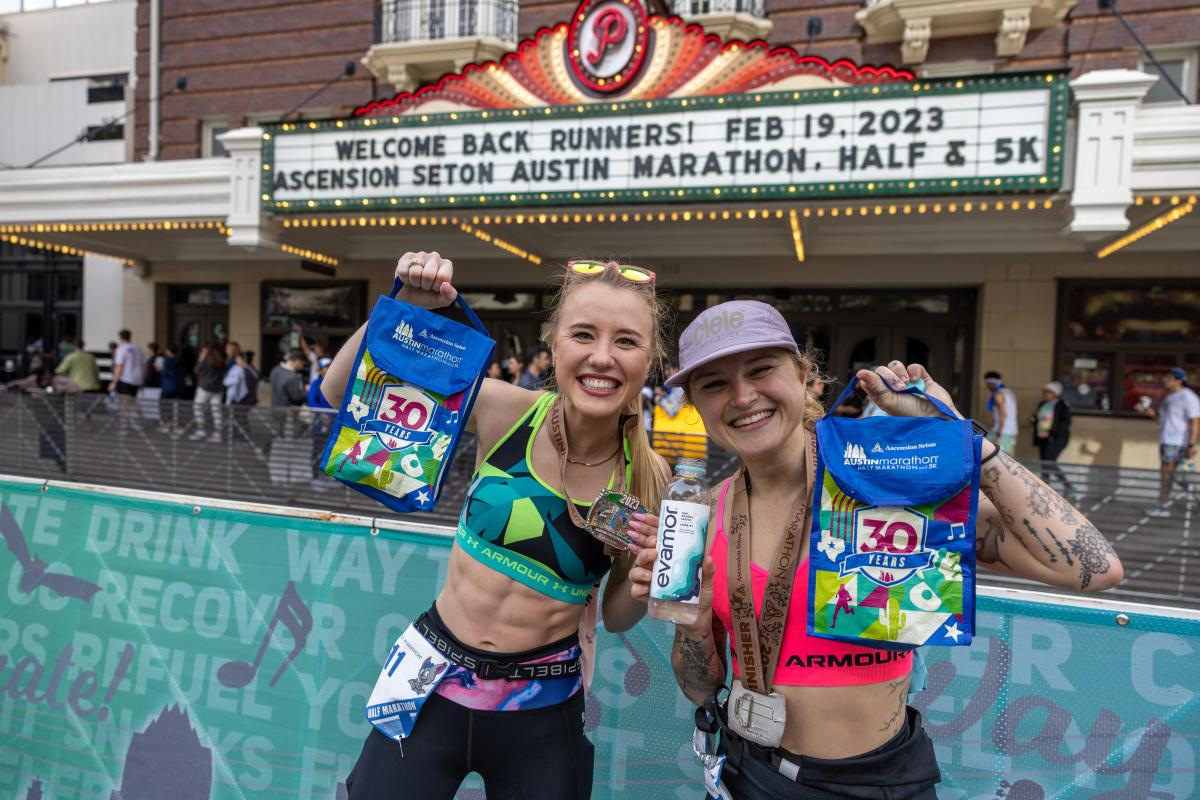 Image of two women at the finish line holding their medals with the Paramount Theater in the background.