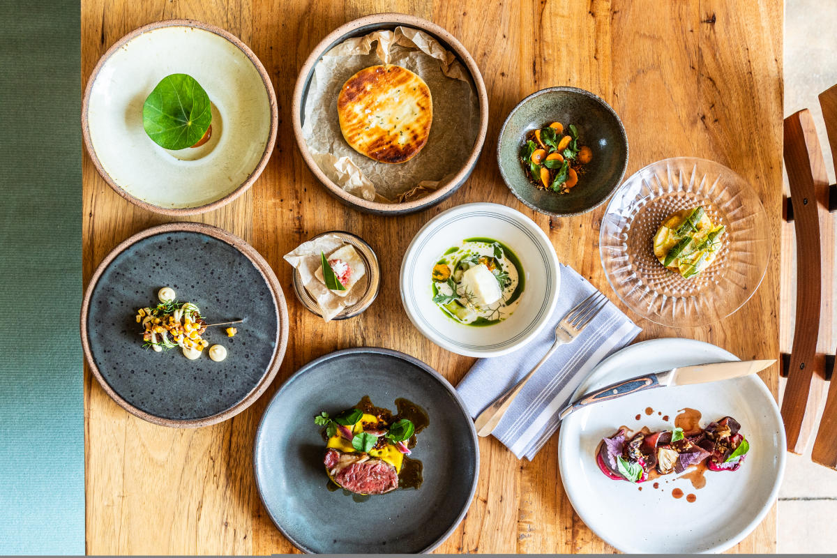 Lay flat image of several different dishes sitting on a wooden table at Barley Swine.