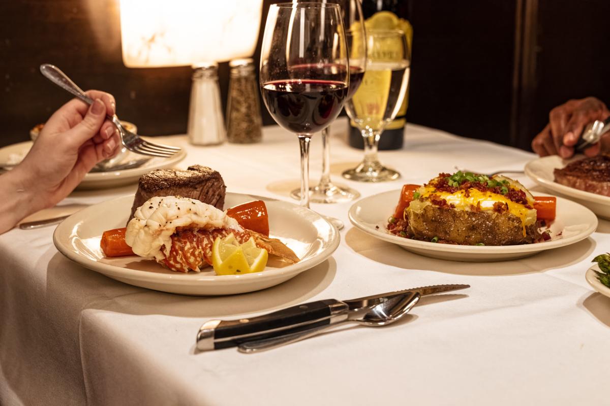 Two plates sitting on a table with people holding forks getting ready to eat.