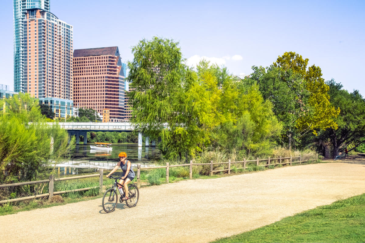 Image of a women biking on the Butler Hike & Bike Trail with Lady Bird Lake and Downtown Austin in the background.