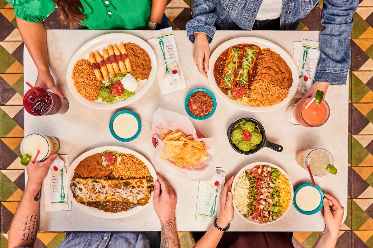 Plates of assorted Tex-Mex entrees and sides on a white table.
