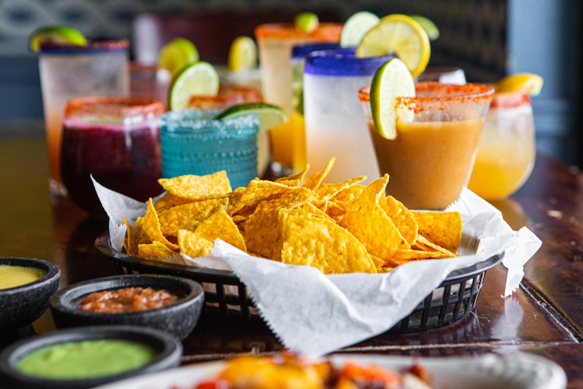 Image of a basket of chips and salsa on a table at Eldorado Cafe with various margaritas and cocktails sitting behind them on the table.