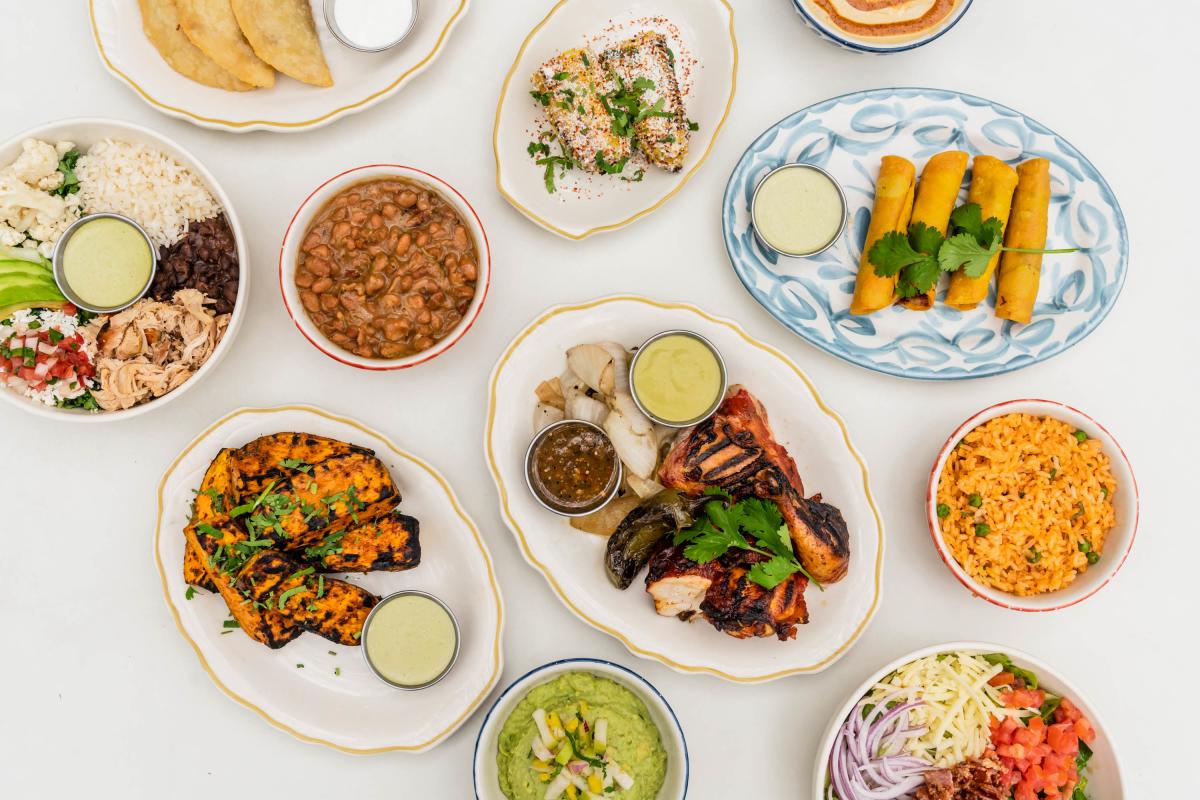 Lay flat image of multiple colorful plates full of food sitting on a white table.