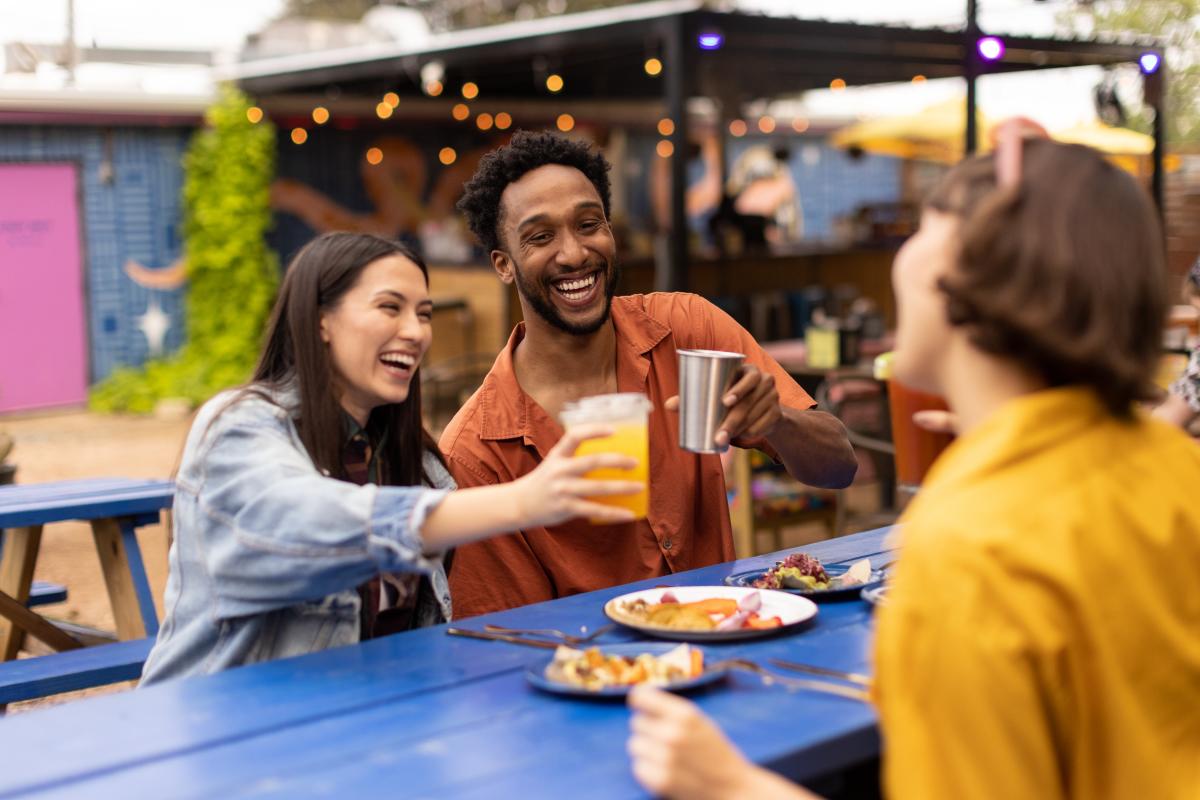 Two women and a man cheering drinks over plates of tacos.