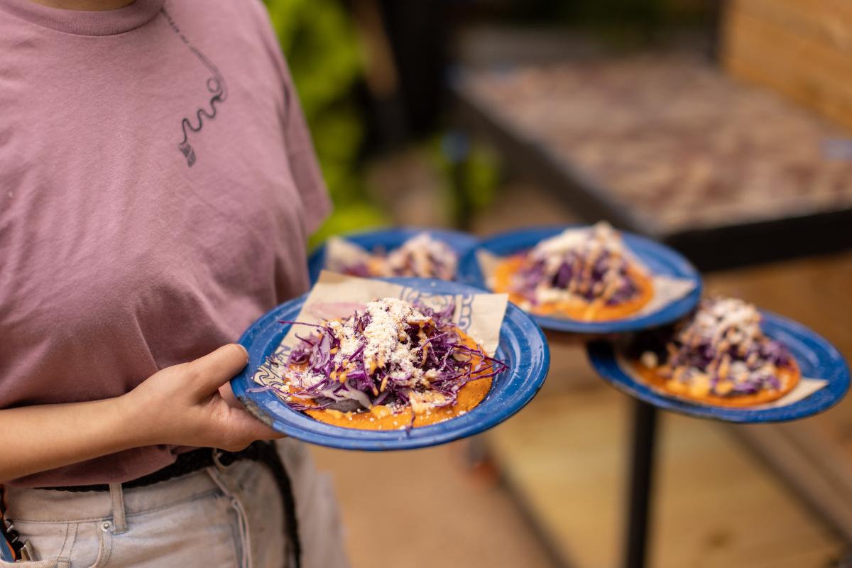 Server carrying three plates of open faced tacos at Nixta Taqueria