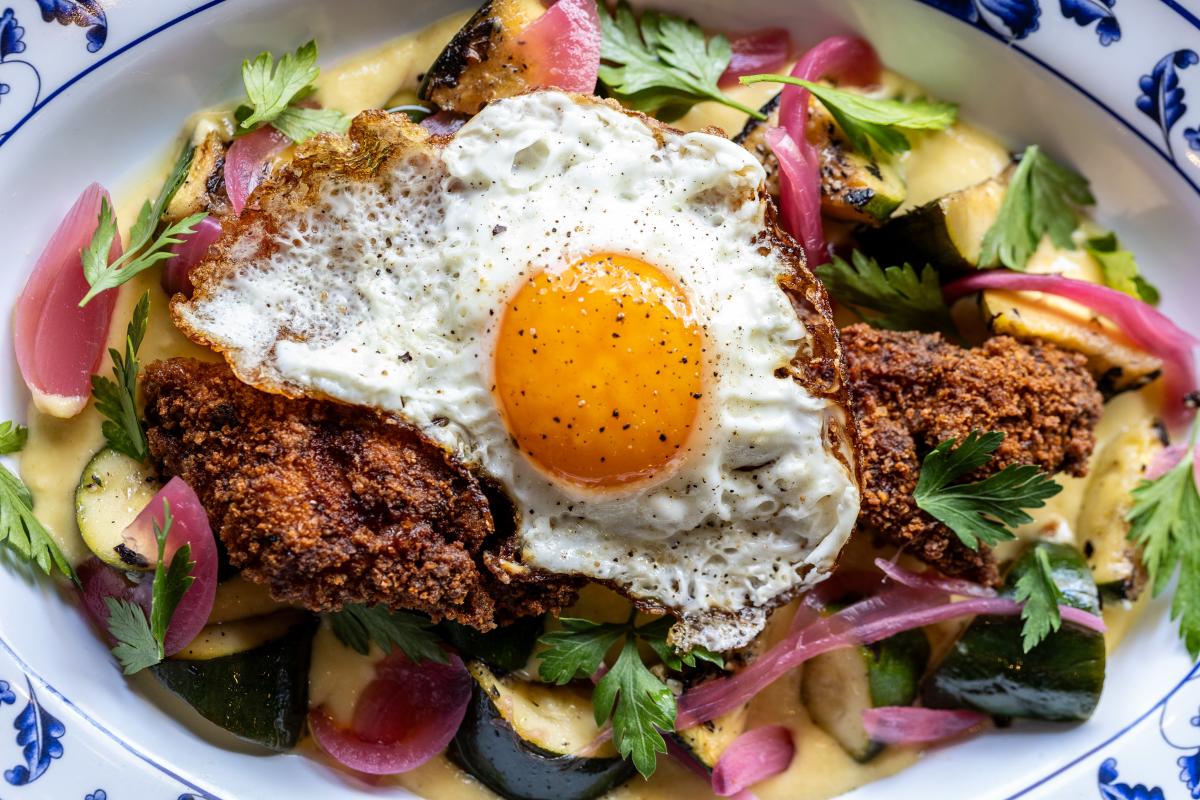 A salad with a fried piece of chicken and sunny-side-up egg on top.