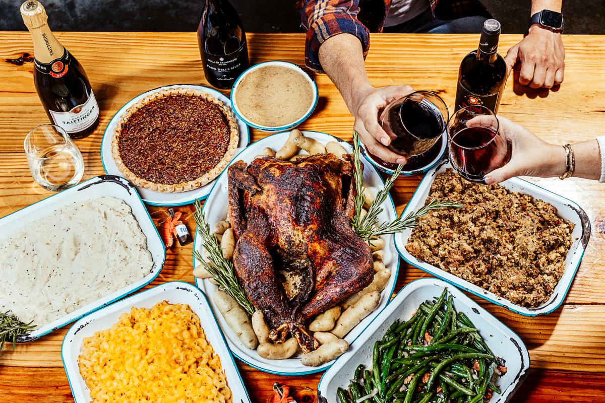 Image of Thanksgiving meal sitting on a table with two hands holding wine glasses.