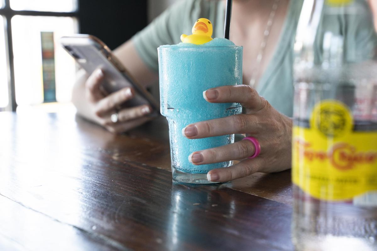 Woman holding blue frozen drink topped with mini, yellow rubber ducky.