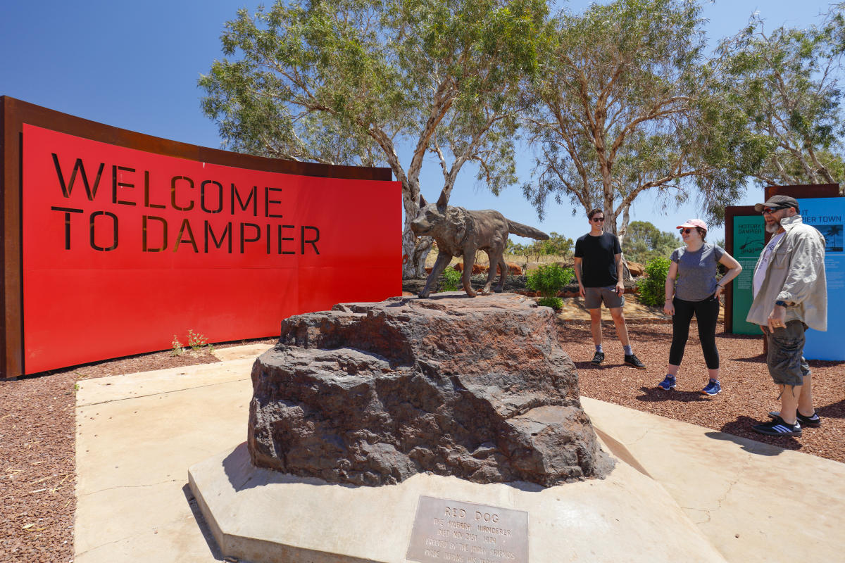 People standing alongside the statue of Red Dog outside Dampier in the Pilbara. This marks the start of the Red Dog Walking Trail