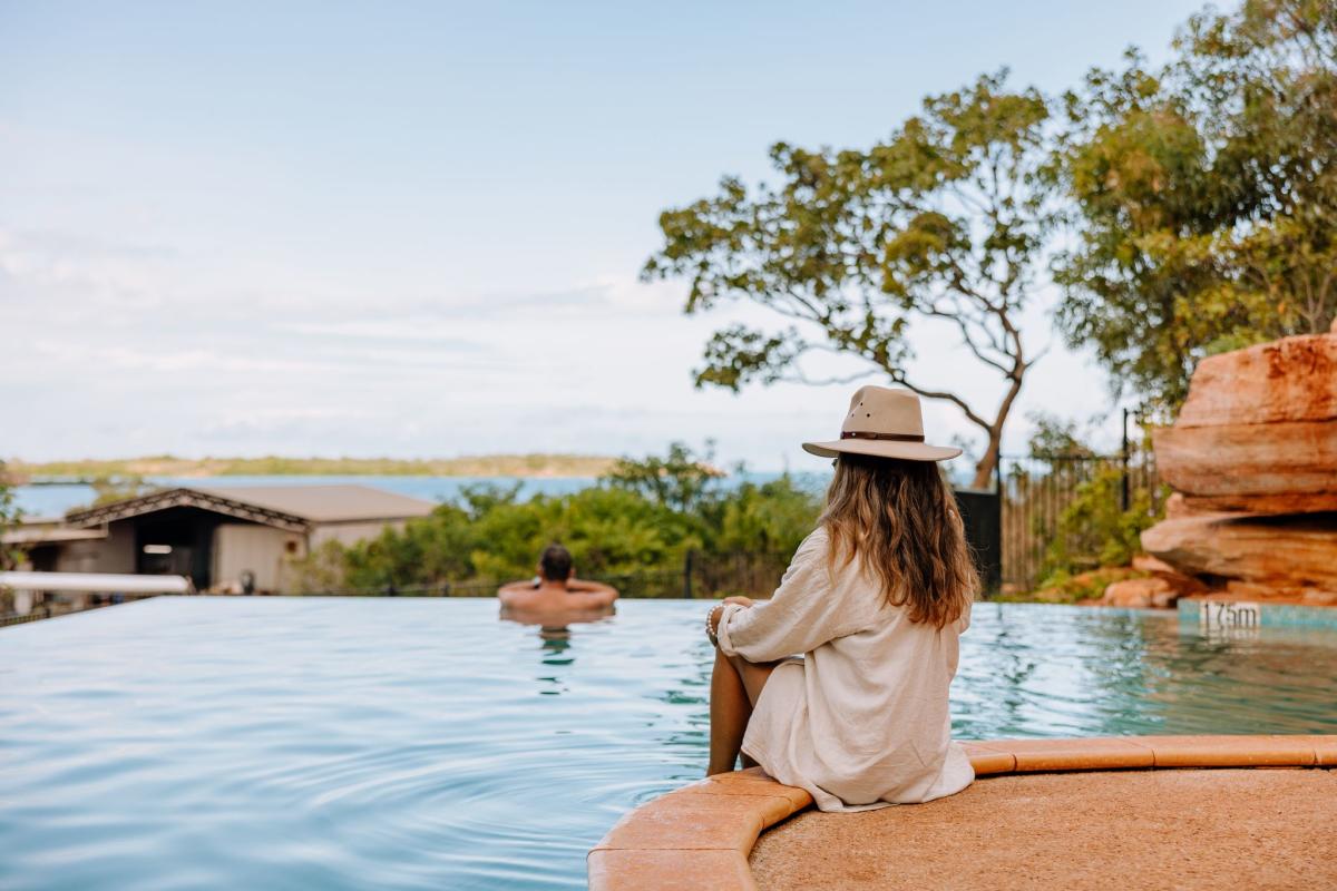 Looking from the swimming pool across to the waters of Cygnet Bay, a man is inside the pool, with a woman sitting on the edge. Both are looking at the view.
